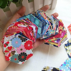 May include: A selection of colourful, hexagonal fabric pieces with floral and geometric patterns. The fabrics feature red, blue, pink, and gold accents. These small fabric pieces are ideal for quilting and crafting projects.