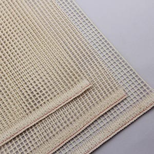 Può includere: Tessuto bianco sporco per aggancio di tappeti con motivo a griglia. Il tessuto è realizzato in materiale tessuto con bordo cucito in rosso. Il tessuto per aggancio di tappeti è mostrato in primo piano.