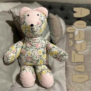 Op de afbeelding: Een handgemaakte teddybeer met een bloemenpatroon in roze, geel en wit. De oren en voeten van de beer zijn effen roze. Naaipatronen worden rechts van de beer weergegeven.