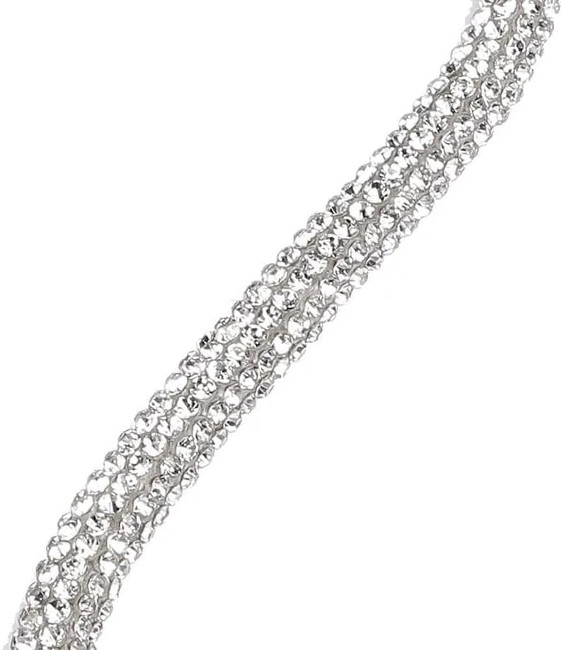 May include: Close-up of a sparkling, silver-toned accessory. The item is densely covered in small, clear crystals, creating a shimmering effect. The design appears to be a strap or band, possibly for a bracelet or necklace, with a diagonal orientation.