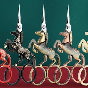 May include: Five decorative scissors with a horse design. Each pair features a different color horse, including red, black, gold, bronze, and cream. The scissors have silver blades and are arranged in a row against a dark green background.