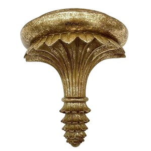 May include: Gold-colored wall shelf bracket with an ornate, classical design. The bracket features a rounded top, a stylized floral motif, and a decorative, cone-shaped base. The finish has a distressed, aged appearance.