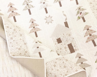Puede incluir: Un edredón blanco con un diseño de patchwork con árboles, una casa y estrellas en tonos marrones, beige y rojo. El edredón tiene un borde blanco y un reverso beige con lunares. El edredón está doblado.