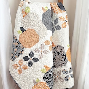 May include: A white quilt with a patchwork design featuring black, orange, and green fabric. The quilt is made up of various geometric shapes and patterns.