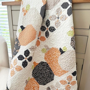 May include: A white quilt with a patchwork design featuring various geometric shapes and floral patterns in shades of orange, black, and green. The quilt is made with a variety of fabrics, including cotton and linen.