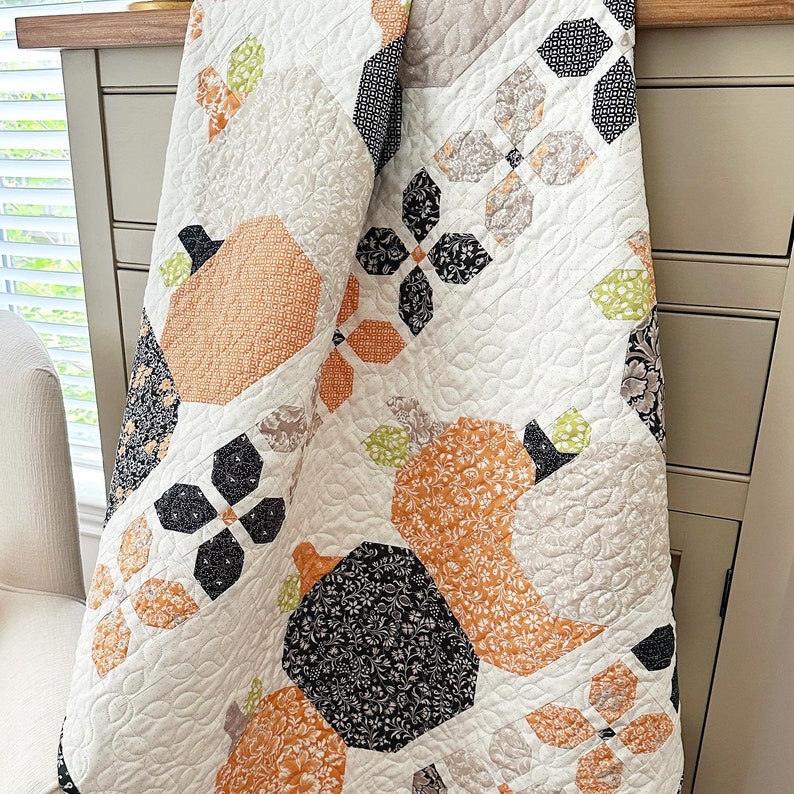 May include: A white quilt with a patchwork design featuring various geometric shapes and floral patterns in shades of orange, black, and green. The quilt is made with a variety of fabrics, including cotton and linen.