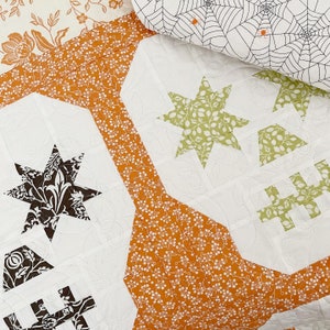 May include: A white fabric quilt with a patchwork design featuring various geometric shapes and floral patterns. The quilt is made with different fabrics in shades of orange, brown, green, and white.