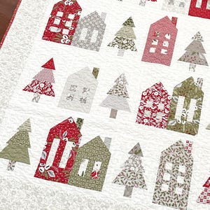 Könnte beinhalten: Eine weiße Steppdecke mit Patchwork-Muster, das rote, grüne und weiße Häuser und Bäume zeigt. Die Häuser haben weiße Fenster und die Bäume haben verschiedene Muster.