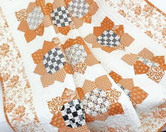 Puede incluir: Una colcha blanca con un diseño de patchwork con cuadrados de tela naranja, negro y blanco. La colcha está hecha de un patrón repetitivo de estrellas de ocho puntas.