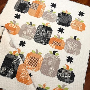 Pode incluir: Um edredom branco com um design de patchwork com abóboras pretas, laranja e cinzas. As abóboras estão dispostas em filas e são acentuadas com estrelas pretas.