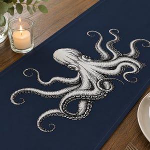 Peut inclure: Un chemin de table bleu marine orné d'une illustration détaillée en blanc, style encre, représentant une pieuvre aux tentacules déployés au centre. Le motif met en valeur la tête de la créature et ses multiples bras à ventouses.