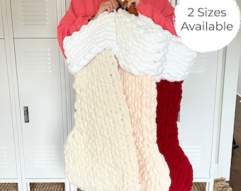 May include: Three chunky knit Christmas stockings in cream, light pink, and deep red, each featuring a thick white cuff. The stockings are made of soft, textured yarn. A circular white graphic overlay in the top right corner displays the text 2 Sizes Available.
