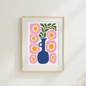 May include: A framed print featuring a stylized floral arrangement. The artwork showcases a navy blue vase holding pink flowers with orange centers and green leaves. The print is set against a white background and framed in a light wood.