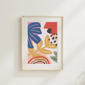 Puede incluir: Impresión artística abstracta en un marco de madera clara. La obra presenta un diseño colorido con formas azules, amarillas, rojas y verdes, incluyendo un arcoíris y elementos florales. El fondo es rosa claro.