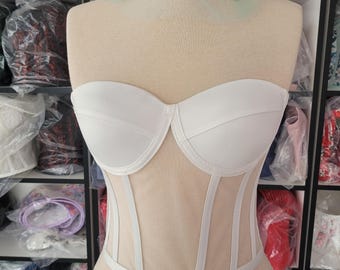 May include: White strapless corset with a sheer mesh panel and vertical seams. The corset is on a white mannequin.