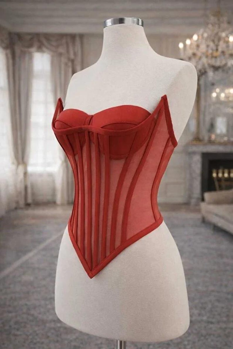 Puede incluir: Un cors&eacute; rojo exhibido en un maniqu&iacute;. El cors&eacute; presenta un corpi&ntilde;o estructurado con ballenas verticales y un escote coraz&oacute;n. El dise&ntilde;o incluye paneles transparentes y un dobladillo en punta, mostrando una mezcla de estructura y detalles delicados.