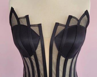 May include: A black strapless corset with a mesh overlay and vertical satin ribbon detailing. The corset has a deep V-neckline and a boned structure.