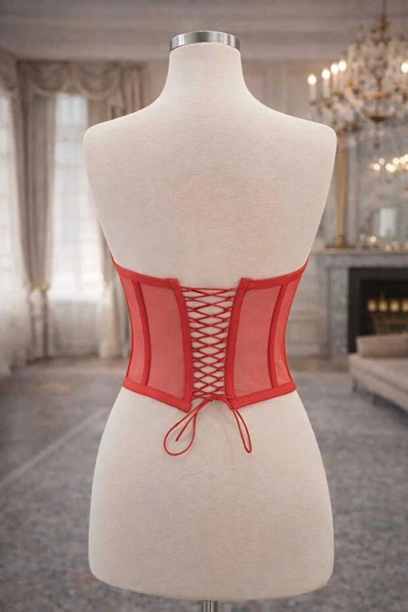 Puede incluir: Un cors&eacute; rojo exhibido en un maniqu&iacute;. El cors&eacute; presenta un dise&ntilde;o de malla transparente con una espalda con cordones. Los bordes est&aacute;n ribeteados con una tela roja lisa. El maniqu&iacute; se encuentra sobre un fondo borroso.