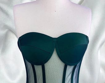 May include: A dark green strapless corset with a mesh panel in the front. The mesh panel has vertical lines.
