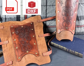 May include: Two brown leather arm guards with decorative Celtic knotwork and brass rivets. The guards are on a dark blue surface with a book.