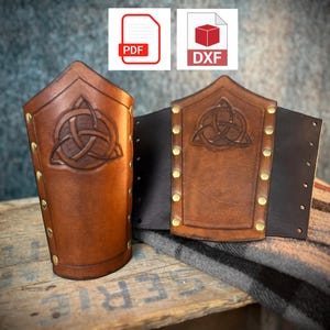 Può includere: Due protezioni per braccia in pelle marrone con un disegno a nodo celtico e rivetti in ottone. Una protezione è in posizione verticale, l'altra è piatta. Lo sfondo include icone PDF e DXF.