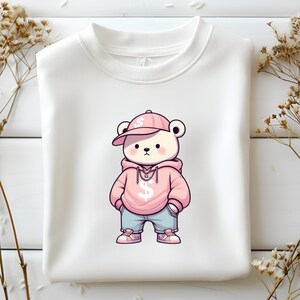 Puede incluir: Una sudadera blanca con un oso de dibujos animados rosa que lleva una sudadera rosa, una gorra de b&eacute;isbol rosa con un signo de d&oacute;lar y pantalones vaqueros azules. El oso sostiene una cadena con un signo de d&oacute;lar.
