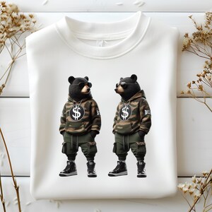 Puede incluir: Sudadera blanca con un estampado gr&aacute;fico de dos osos negros con sudaderas con capucha de camuflaje y gafas de sol. Los osos sostienen signos de d&oacute;lar y el texto "DIS" y "BIG" es visible en sus sudaderas con capucha.
