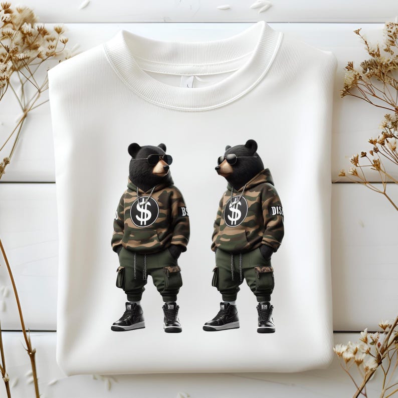 Puede incluir: Sudadera blanca con un estampado gr&aacute;fico de dos osos negros con sudaderas con capucha de camuflaje y gafas de sol. Los osos sostienen signos de d&oacute;lar y el texto "DIS" y "BIG" es visible en sus sudaderas con capucha.