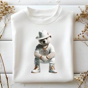 Puede incluir: Sudadera blanca con un gr&aacute;fico de un oso blanco que lleva un sombrero blanco, una cadena de oro y un reloj de oro. El oso est&aacute; sentado con las piernas cruzadas y lleva zapatillas blancas.