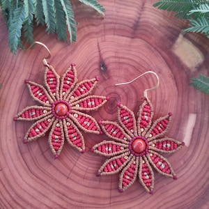 Peut inclure: Une paire de boucles d'oreilles en macramé rouge et or avec une pierre rouge au centre de chaque fleur.