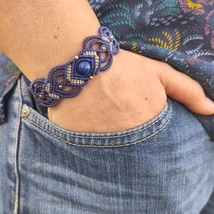Peut inclure: Un bracelet en macramé bleu et beige avec une pierre précieuse bleu foncé au centre.
