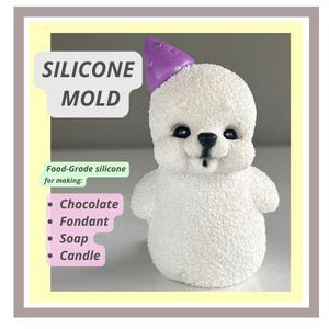 May include: A white silicone mould shaped like a seal wearing a purple party hat. The mould is for making chocolate, fondant, soap, or candles. The text "SILICONE MOLD" is written in black on a white background.