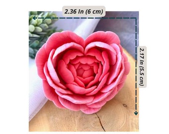 May include: A pink, heart-shaped flower with detailed petals, measuring 2.36 inches (6 cm) wide and 2.17 inches (5.5 cm) tall. The flower is set on a wooden surface, with a white fabric and green plant in the background.