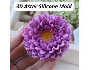 May include: A 3D Aster Silicone Mold featuring a detailed flower shape with numerous purple petals surrounding a textured yellow center. The text 3D Aster Silicone Mold is clearly visible at the top of the image, identifying the product.