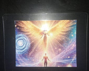 May include: A rectangular print featuring a celestial scene with a glowing winged figure hovering above a silhouette of a person. The background displays a vibrant cosmic nebula with swirling blue and purple energy patterns and bright golden light.