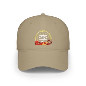Puede incluir: Gorra de béisbol beige con un emblema circular que contiene caracteres chinos y las palabras "resiliencia, elegancia, integridad". El emblema está rodeado de diseños florales rojos y amarillos. La gorra tiene una visera curva.