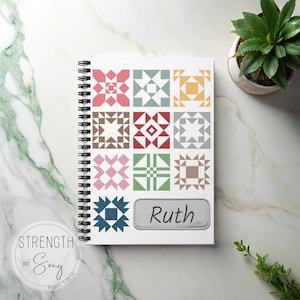 May include: A spiral-bound notebook with a white cover displaying a colourful quilt block pattern. The notebook has a grey label with the name "Ruth" and a circular logo with the words "Strength and Song". A small potted plant is visible.