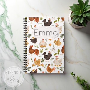 May include: A spiral-bound notebook with a white cover featuring a pattern of colourful chickens and foliage. The name "Emma" is displayed in a grey oval. The notebook is on a marble surface, with a small potted plant visible.