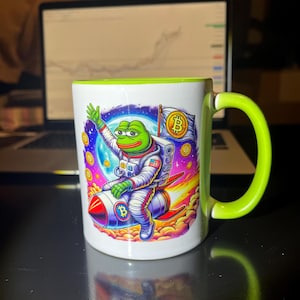 Peut inclure: Une tasse en céramique blanche avec un bord et une poignée verts. La tasse présente un motif coloré d'une grenouille verte portant une combinaison d'astronaute et chevauchant une fusée. La grenouille tient un drapeau avec un symbole Bitcoin. L'arrière-plan est une scène spatiale psychédélique avec des étoiles et des planètes.