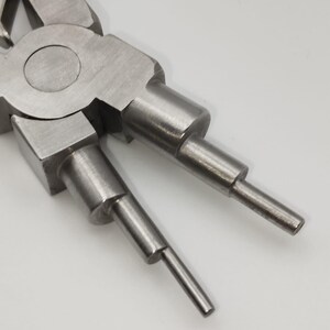 May include: Close-up of a metal ring pliers tool with blue handles. The pliers have a silver finish and are designed with two pointed tips for gripping and manipulating rings. The tool is designed for precision work.