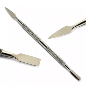 Puede incluir: Una herramienta para cutículas plateada de doble extremo con un mango texturizado. Un extremo presenta una hoja puntiaguda y el otro un borde plano en forma de espátula. También se muestran vistas de primer plano adicionales de la herramienta.