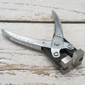 Puede incluir: Alicates de metal plateado con mango negro y una mandíbula texturizada. Los alicates tienen una escala en el mango.