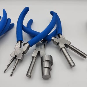 Könnte beinhalten: Eine Sammlung von Metall-Schmuckzangen mit blau gepolsterten Griffen. Die Zangen haben verschiedene Formen und Größen, darunter Rundzangen, Flachzangen und Stufenzangen. Die Werkzeuge sind für die Schmuckherstellung und das Basteln konzipiert.