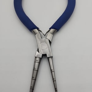 May include: A pair of silver metal pliers with blue rubber handles. The pliers have tapered tips with numbered markings, ranging from 2 to 8. The tool is designed for precision work and is set against a plain white background.