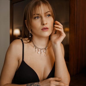 May include: A silver-toned chain necklace featuring multiple dangling white baroque pearls and small metallic charms. The necklace rests at the base of the neck and is paired with matching drop earrings featuring a single white pearl on a thin chain.