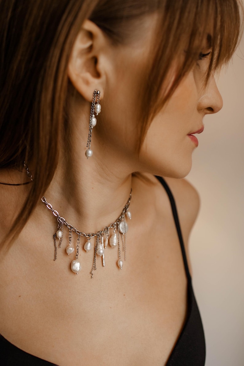 May include: A silver-toned chain necklace featuring multiple dangling white freshwater pearls of varying shapes and sizes, paired with a matching drop earring consisting of a silver chain and small white pearls hanging from a stud post.