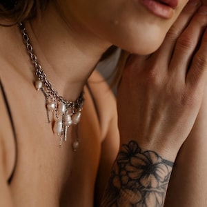 May include: A silver-toned chain necklace featuring multiple dangling white baroque pearls of irregular shapes. The necklace consists of interconnected metal links with several pearl charms suspended at varying lengths along the front of the chain.