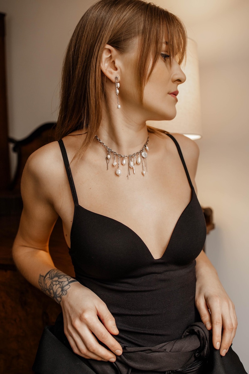 May include: A silver-toned chain necklace featuring multiple dangling white baroque pearls and thin metal accents, paired with matching drop earrings that consist of a silver chain and a single white baroque pearl at the end of each piece.