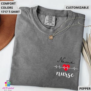 May include: A pepper-colored Comfort Colors 1717 t-shirt featuring a graphic on the lower right side with the word Name in black script, a red heart with a white heartbeat line, and the word nurse in white script below the heart.
