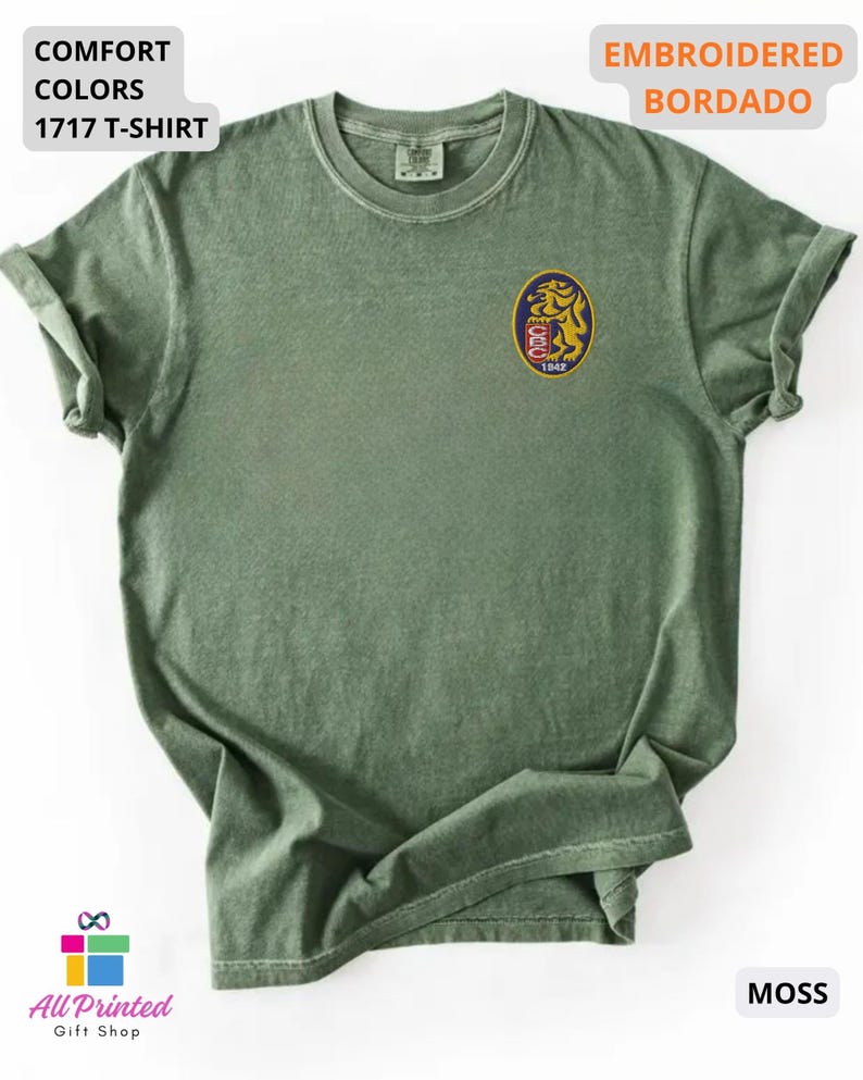 Mockup of a Comfort Colors 1717 vintage-colored t-shirt featuring a small embroidered Venezuela-inspired lion crest on the left chest. The embroidery showcases a gold lion inside a navy blue oval with red and white shield details and the year 1842. A close-up view of the embroidered design is displayed alongside the shirt, highlighting the textured stitching and premium craftsmanship. Ideal Venezuelan pride apparel, Venezuela gift, VZLA shirt, and Caracas-inspired clothing.